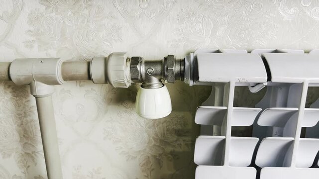 thermostatic radiator valve with adjustable white knob on metal pipe fitting against floral embossed wallpaper