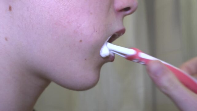 Brushing teeth nearby.A close-up of a person's face from the side while brushing their teeth with a red and white toothbrush with white foaming paste highlights the importance of daily oral hygiene.