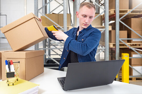 Warehouse operations, order fulfillment. Employee scans parcel barcode at packing station using handheld reader and laptop, updating inventory, preparing shipment, or e-commerce distribution.