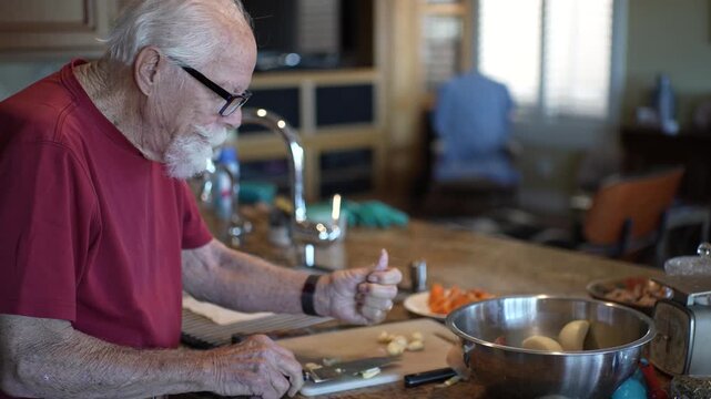 Senior man skillfully mashes and minces garlic in home kitchen while following a recipe for his meal preparation.