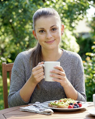 A young pretty woman with a ponytail having breakfast in the garden on a summer day