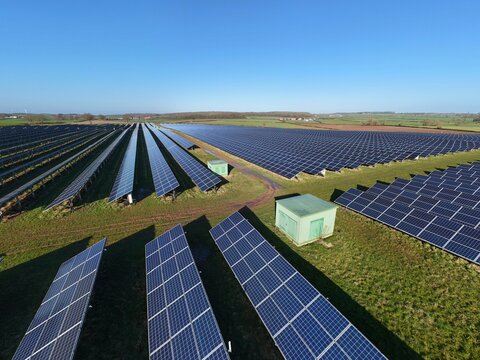 Aerial view of rows of solar panels basking under a clear sky, generating clean energy amidst the green fields, Retford, United Kingdom.