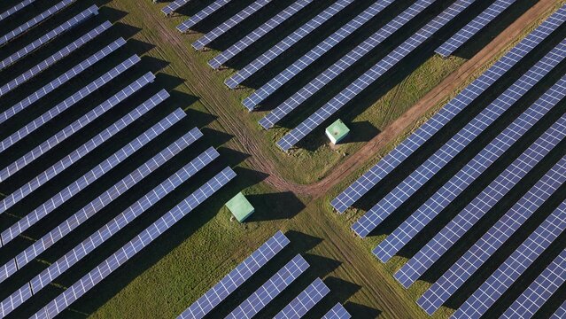 Aerial view of rows of solar panels glinting in the sunlight, a geometric dance of dark blue against the bright green fields, Retford, United Kingdom.