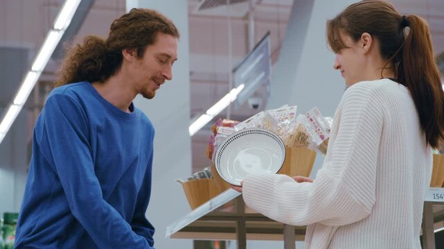 Husband and wife choosing new teapot and plates while shopping together in a large retail store
