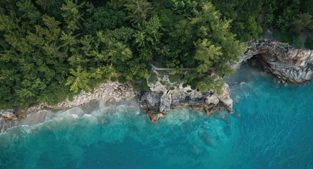 Fototapeta premium Overhead perspective of a rugged coastline with dense green foliage and clear summer beach