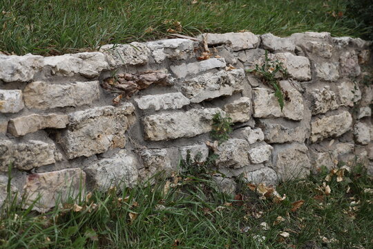 quarried limestone block landscaping wall with green grass, autumn leaves (close-up)