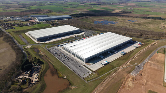 Aerial view of sprawling industrial warehouses reflecting the diffused sunlight, surrounded by vast fields, Doncaster, Doncaster, United Kingdom.