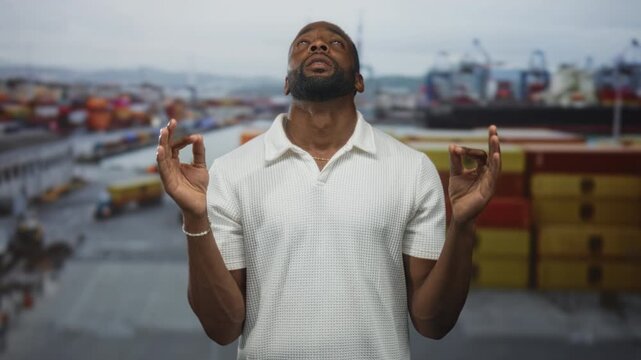 Man with hands pressed in prayer at busy port terminal, looking up toward sky in white shirt; faith devotion serenity.