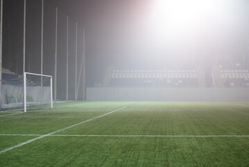 Fototapeta premium Foggy indoor soccer field with goalpost and empty spectator seating