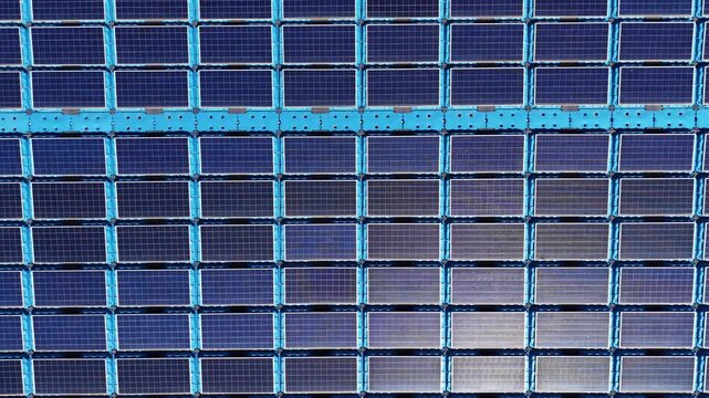 Rising top-down aerial of floating photovoltaic array on lined reservoir, with modular pontoons and DC strings generating power while reducing water evaporation and algae growth