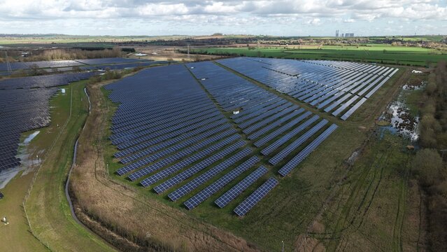 Aerial view of solar panels glinting under a vast sky, juxtaposed against the earthy tones of the surrounding landscape, Tiln Battery Energy Storage System, Retford, United Kingdom.