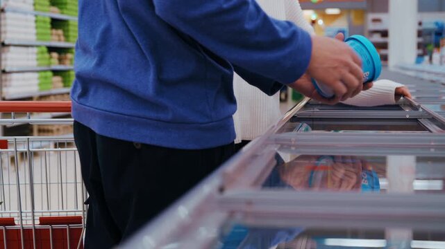 A man and woman stand before open freezer cases, pulling out frozen vegetables and ready meals for closer inspection. 