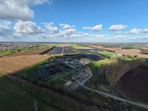 Aerial view of a wastewater treatment plant nestled among solar farms, contrasting with the surrounding golden fields under a vast sky, Worksop, United Kingdom.