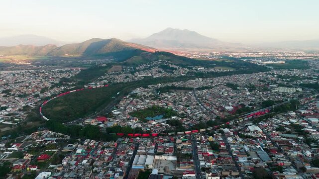 Aerial view of a red cargo train winding through the city of tepic, mexico with mountains nearby
