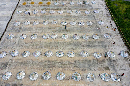 Aerial view of rows of conical hats drying in the sun, creating a mesmerizing pattern on the vast open ground, Brahmanbaria, Chittagong Division, Bangladesh.