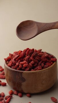 Dried Goji berries or Wolfberry falling from a spoon on a wooden bowl.