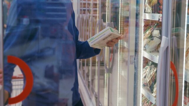 In the refrigerated section of a grocery store, a couple reaches into a freezer to grab bags of frozen fruit and vegetables. 