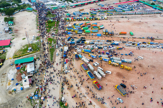 Aerial view of bustling crowds mingling amidst a vibrant array of parked trucks and buses, creating a tapestry of commerce and transit, Mawa, Dhaka Division, Bangladesh.