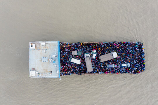 Aerial view of a ferry packed with people and vehicles contrasts sharply with the surrounding muddy waters, Mawa, Dhaka Division, Bangladesh.