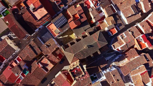 Many houses with tiled roofs are seen from above, displaying a mix of colors and shapes. Narrow streets weave between the buildings in a dense layout typical of a small town setting.