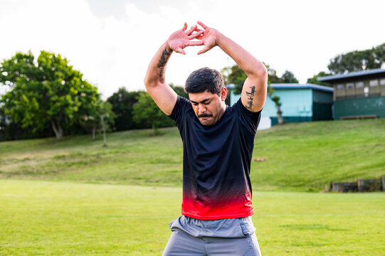 Samoan man doing haka dance moves with arms over his head in grass field