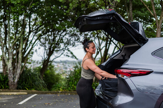 Mixed race woman unloading sports bag from open car boot at parking area