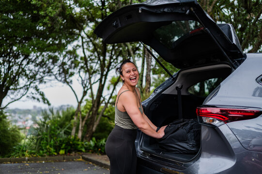 Mixed race woman unloading sports bag from open car boot at parking area