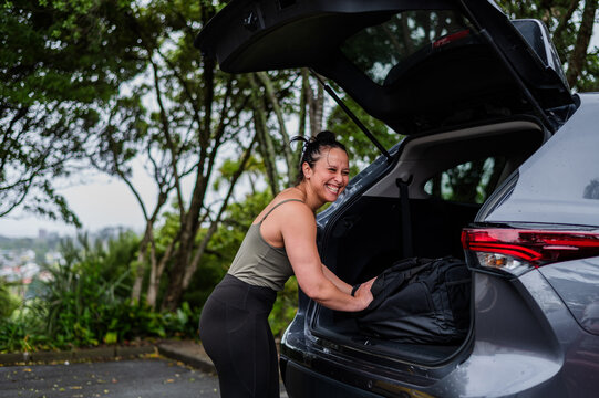 Mixed race woman unloading sports bag from open car boot at parking area