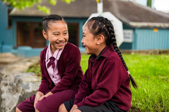 Two Samoan school kids sitting on a stone ledge outdoors
