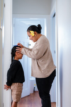 Young Samoan boy with braided hair standing against the wall while mum measures his height