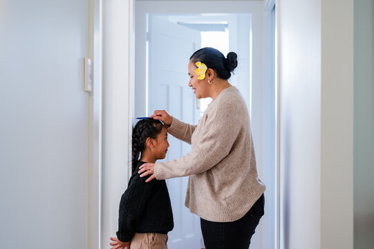Young Samoan boy with braided hair standing against the wall while mum measures his height