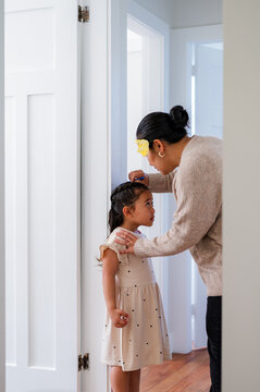 Young Samoan girl standing against the wall while mum measures her height