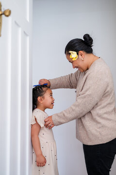 Young Samoan girl standing against the wall while mum measures her height