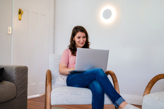 Italian woman sitting on a lounge chair working on her laptop inside home