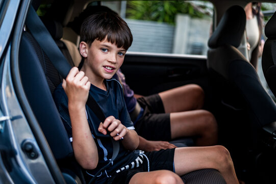 Young boy seated on backseat with older brother fastens his seatbelt