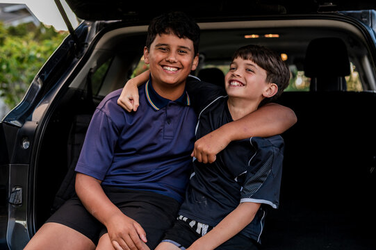 Two boys sitting in an open car boot with arms over each others shoulder