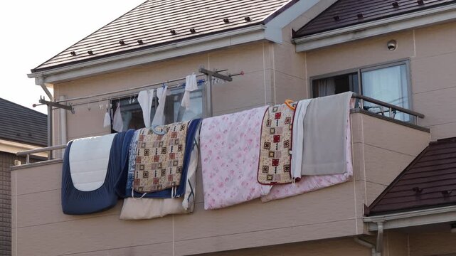 風に揺れる住宅の2階に干した布団と洗濯物