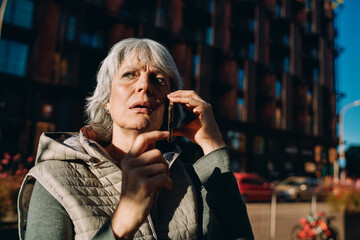 Mature woman walks confidently while holding smartphone, capturing the rhythm of modern mobility and spontaneous use of mobile tech in urban environment. © BullRun