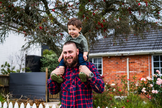 Man in red plaid shirt carrying toddler son on his shoulders outdoors