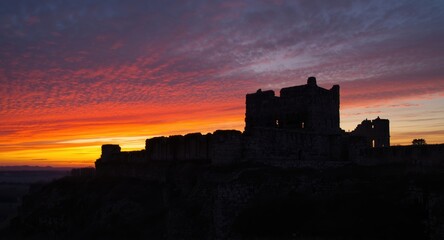 Obraz premium Ancient castle ruins silhouetted against a vibrant sunset emphasizing historical depth and structural beauty