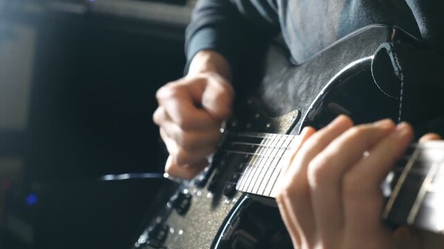 Close up fingers of guitarist at the strings. Mens arms plays solo of rock music. Hands of male musician playing at electric guitar. Beautiful black background at studio. Slow motion Close up