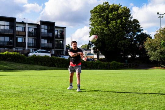 Maori man throwing a rugby ball on a green field at a local park