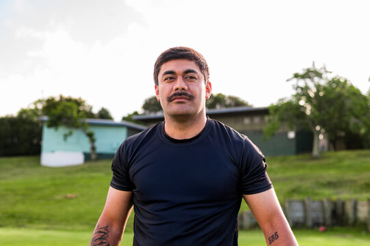 A man wearing a sports shirt stands confidently on a grassy field under a bright sky