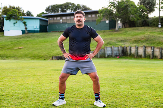 A male athlete in training stance, preparing for a workout on a grassy field in a park setting