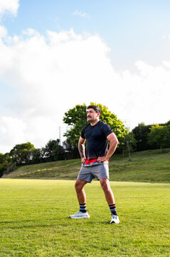 Samoan man doing haka dance moves with arms on his waist in grass field