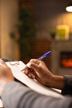 Professional therapist taking notes during counseling session, evaluating mental health assessment of client. African American psychologist writing in notepad, providing supportive therapy services.