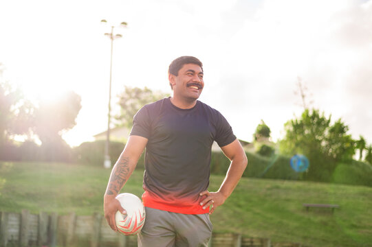 A happy man with a rugby ball in a sunny park, showcasing confidence and joy