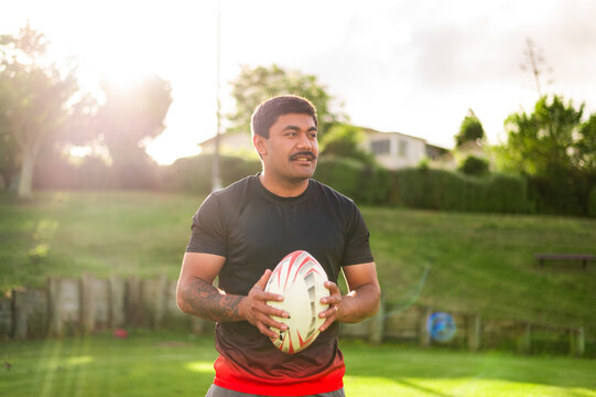 A man holds a rugby ball and gets ready for practice in a sunny park