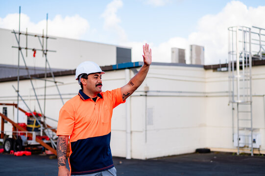 A man in work attire waving his hand at a construction site under a clear sky