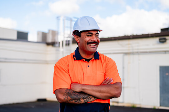 A man in safety gear stands with crossed arms, smiling at the work site